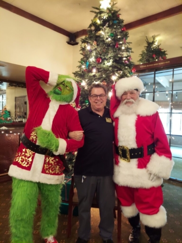 The Grinch, Steve Jennings (Community Liaison), and Santa pose in front of the Christmas tree at The Oaks of Pasadena