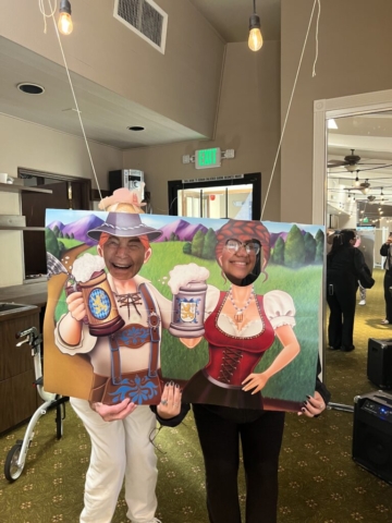 Residents enjoying Oktoberfest festivities at The Oaks of Pasadena senior apartments, posing with a themed photo cutout board