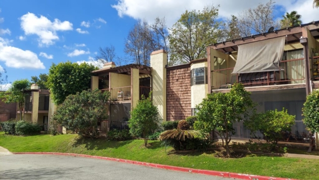 Exterior view of the west two-story apartment building at The Oaks of Pasadena on a beautiful sunny day with puffy clouds in the sky