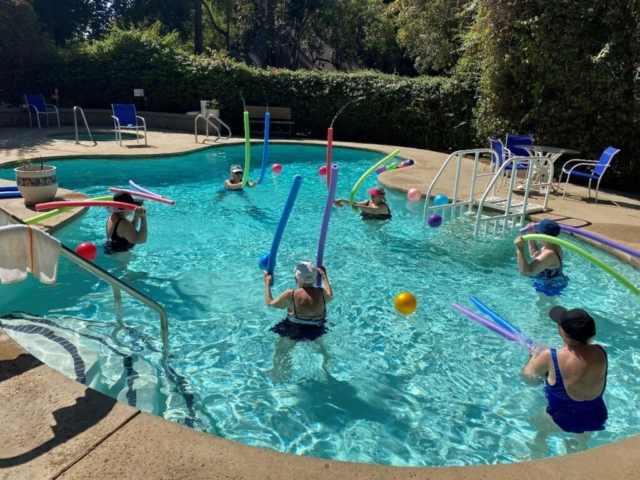 Residents enjoying a weekly summer pool exercise class in the heated outdoor pool at The Oaks of Pasadena senior living community.