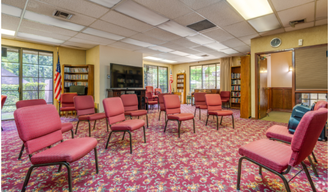 Spacious activities room at The Oaks of Pasadena senior living community, featuring a lending library, big-screen TV, and setup for daily exercise classes